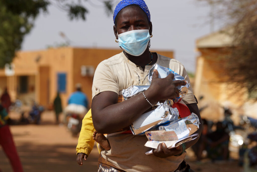 Una donna beneficiaria cammina nel luogo di distribuzione dove ha ricevuto una razione di SuperCereal, una farina infantile fortificata, utilizzata per prevenire la malnutrizione tra i bambini dai 6 ai 23 mesi. Crediti: WFP/Esther Ouoba